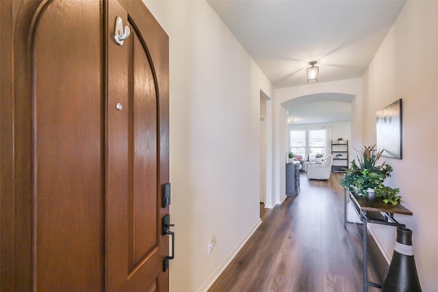 entrance foyer featuring arched walkways, dark wood-style flooring, and baseboards