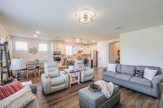 living room with dark wood-style flooring, visible vents, recessed lighting, and arched walkways