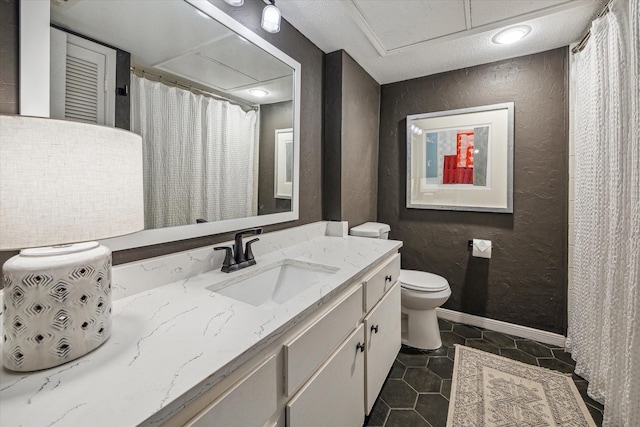 bathroom with toilet, baseboards, tile patterned floors, vanity, and a textured wall