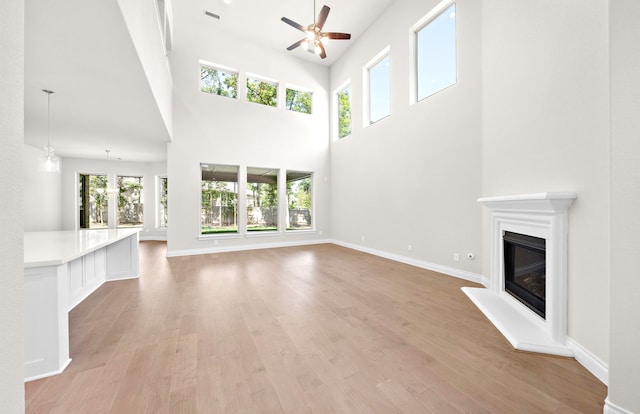 10719 Jacobina Ct, Cypress, TX 77433 - unfurnished living room with light wood finished floors, a high ceiling, a glass covered fireplace, a ceiling fan, and visible vents