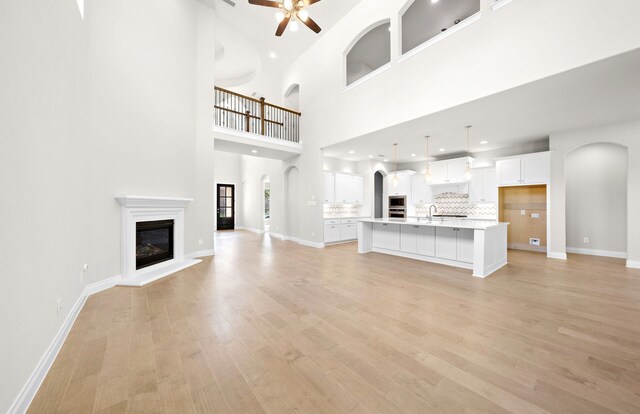 10719 Jacobina Ct, Cypress, TX 77433 - unfurnished living room featuring light wood-style floors, baseboards, arched walkways, a glass covered fireplace, and a ceiling fan