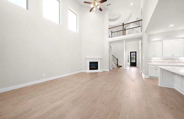 10719 Jacobina Ct, Cypress, TX 77433 - unfurnished living room with a high ceiling, stairway, ceiling fan, a glass covered fireplace, and light wood-style flooring