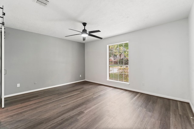 empty room with dark wood-style floors, a ceiling fan, visible vents, and baseboards