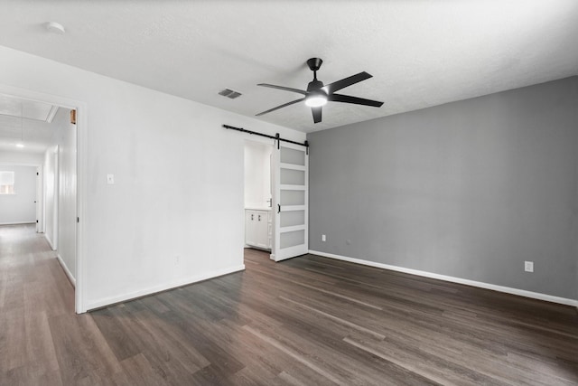 spare room featuring attic access, a barn door, a ceiling fan, and dark wood finished floors