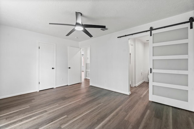 unfurnished bedroom with a barn door, ceiling fan, visible vents, a textured ceiling, and wood finished floors