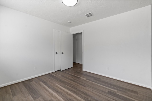 unfurnished room featuring a textured ceiling, visible vents, baseboards, and dark wood finished floors