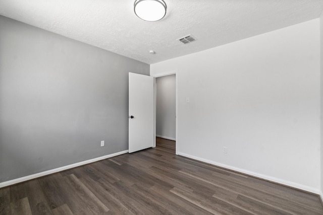 spare room featuring dark wood-type flooring, visible vents, a textured ceiling, and baseboards