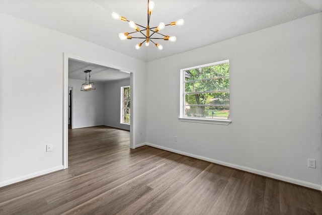 empty room featuring a notable chandelier, wood finished floors, and baseboards