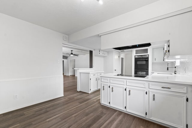 kitchen featuring dark wood-style floors, a sink, black appliances, a peninsula, and white cabinets