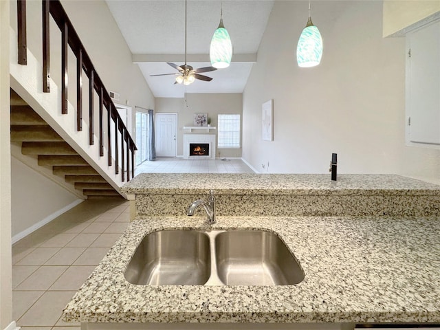 kitchen with a sink, light tile patterned floors, ceiling fan, light stone counters, and lofted ceiling