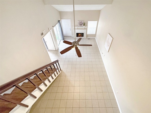 interior space with a ceiling fan, visible vents, a lit fireplace, baseboards, and tile patterned flooring