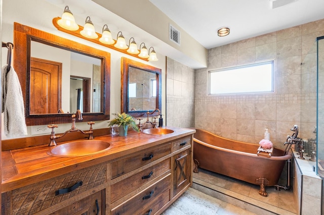 11008 Hillside Dr, Willis, TX 77318 - bathroom featuring double vanity, visible vents, a freestanding bath, tile walls, and a sink