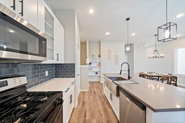 kitchen with light wood finished floors, a kitchen island with sink, a sink, stainless steel appliances, and decorative backsplash