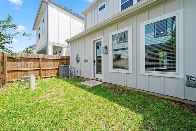 rear view of house with cooling unit, a yard, board and batten siding, and fence