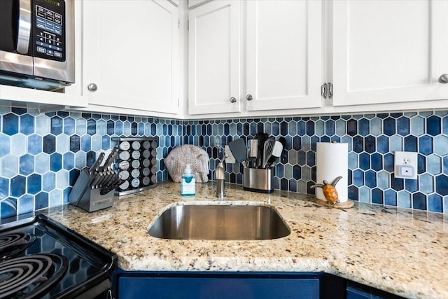kitchen with stainless steel microwave, tasteful backsplash, white cabinets, and a sink