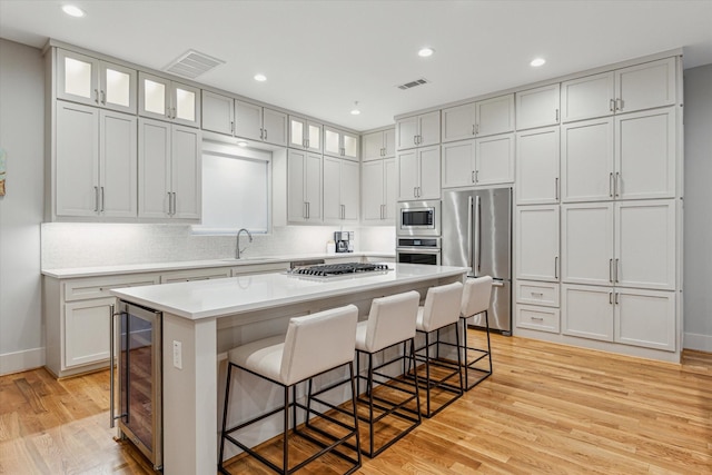 kitchen featuring light wood finished floors, stainless steel appliances, wine cooler, a breakfast bar area, and baseboards