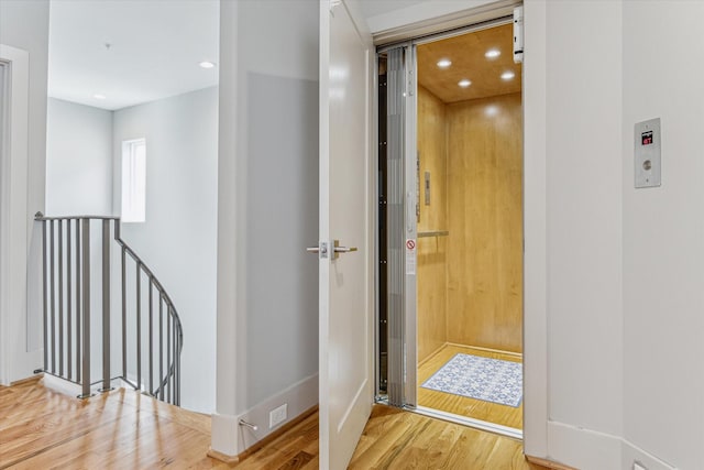 corridor featuring recessed lighting, an upstairs landing, wood finished floors, and elevator