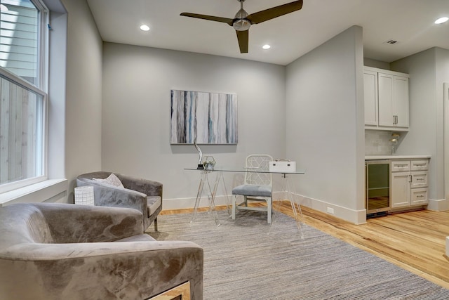 living area with beverage cooler, ceiling fan, baseboards, recessed lighting, and light wood finished floors