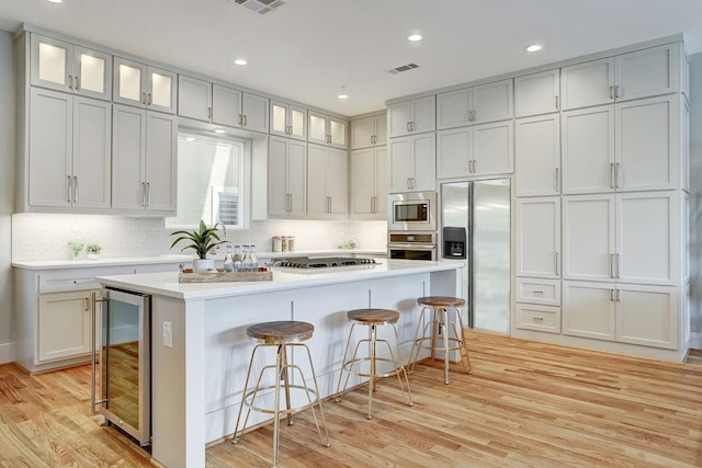 kitchen with a kitchen breakfast bar, built in appliances, visible vents, light wood-style floors, and wine cooler