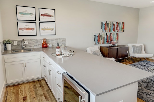 bar with beverage cooler, tasteful backsplash, light wood finished floors, and a sink