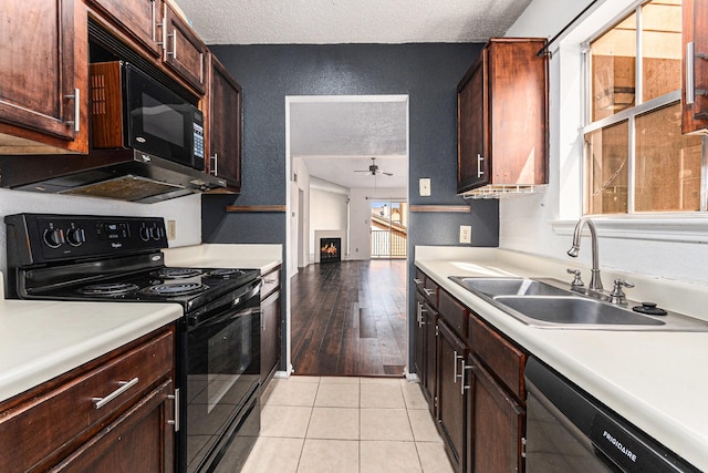 kitchen with a sink, ceiling fan, black appliances, a textured wall, and light countertops