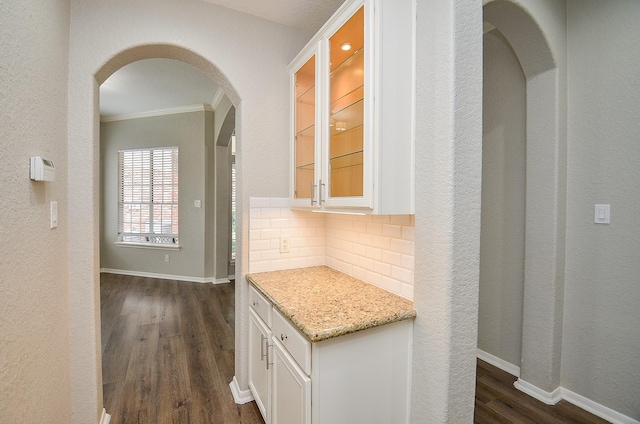 corridor featuring baseboards, ornamental molding, dark wood-style floors, and arched walkways
