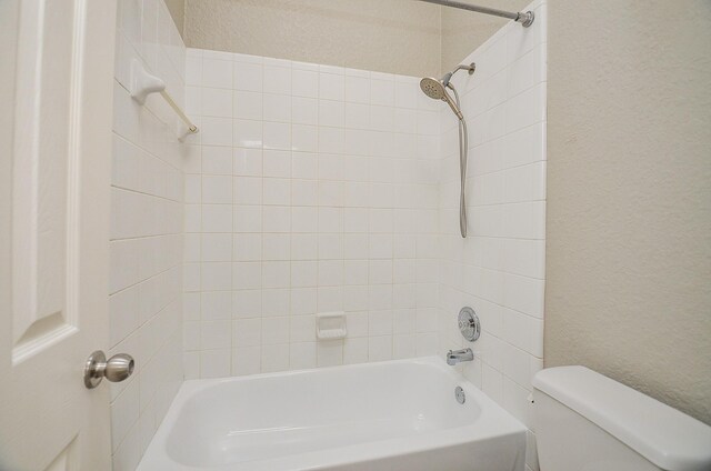 bathroom featuring toilet, a textured wall, and shower / bathing tub combination