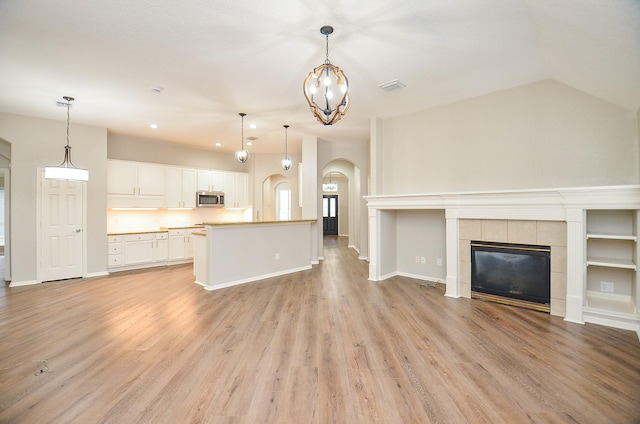 unfurnished living room with a chandelier, light wood-type flooring, visible vents, baseboards, and arched walkways