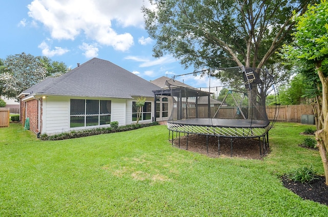 rear view of house featuring a lawn, a fenced backyard, and a trampoline