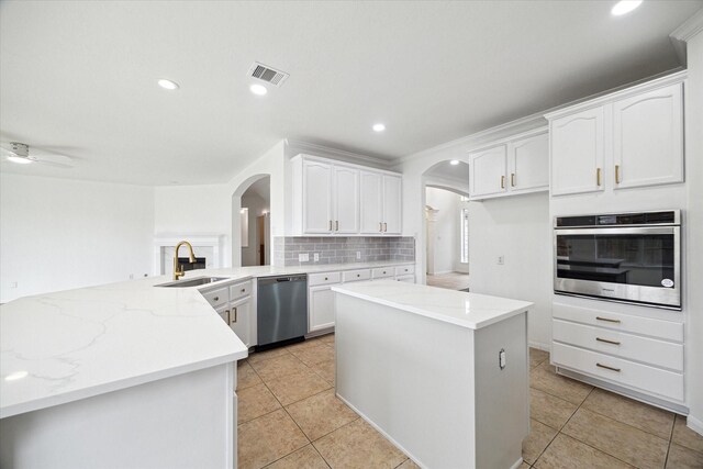kitchen featuring light stone counters, white cabinets, a sink, appliances with stainless steel finishes, and arched walkways