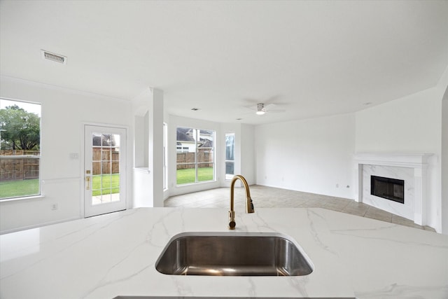 kitchen featuring a sink, a ceiling fan, visible vents, light stone counters, and open floor plan