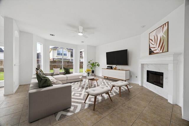 tiled living room featuring visible vents, a ceiling fan, a premium fireplace, and plenty of natural light