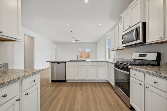 kitchen with a sink, stainless steel appliances, light wood-type flooring, a peninsula, and white cabinets