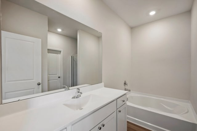 bathroom with a garden tub, a stall shower, recessed lighting, wood finished floors, and vanity