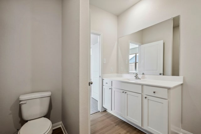 half bathroom with baseboards, wood finished floors, toilet, and vanity