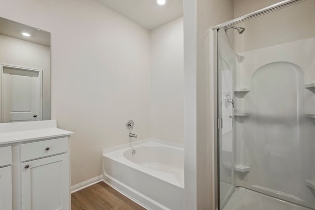 bathroom featuring a shower stall, a garden tub, baseboards, wood finished floors, and vanity