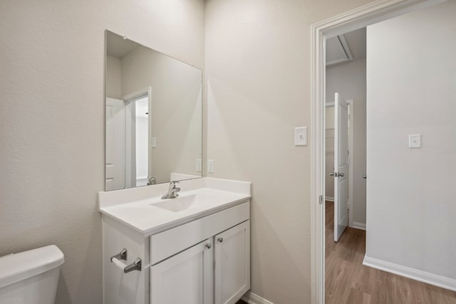 half bath with toilet, vanity, wood finished floors, and baseboards