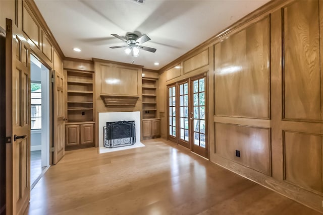 unfurnished living room with crown molding, a ceiling fan, built in shelves, a fireplace with flush hearth, and light wood finished floors