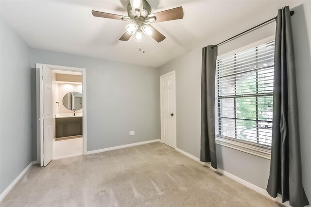 unfurnished bedroom featuring light colored carpet, connected bathroom, baseboards, and ceiling fan