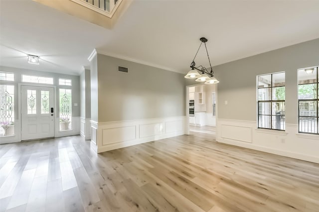 unfurnished dining area with visible vents, ornamental molding, a decorative wall, light wood-style floors, and a wainscoted wall