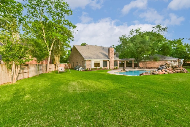 back of property featuring a fenced backyard, a chimney, a fenced in pool, brick siding, and a yard