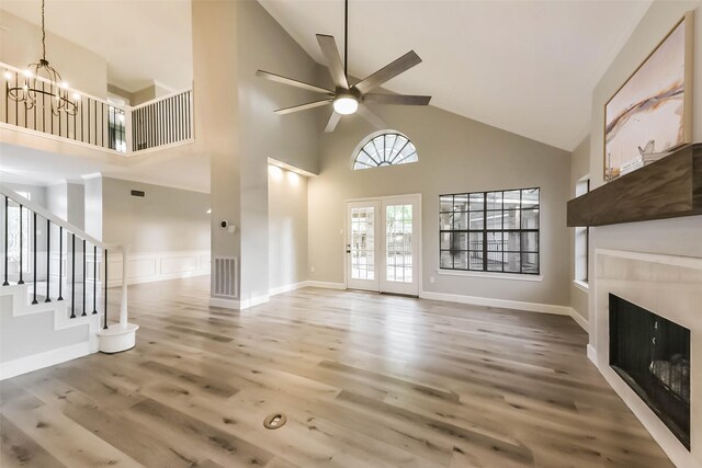unfurnished living room featuring visible vents, wood finished floors, high vaulted ceiling, a tile fireplace, and ceiling fan with notable chandelier