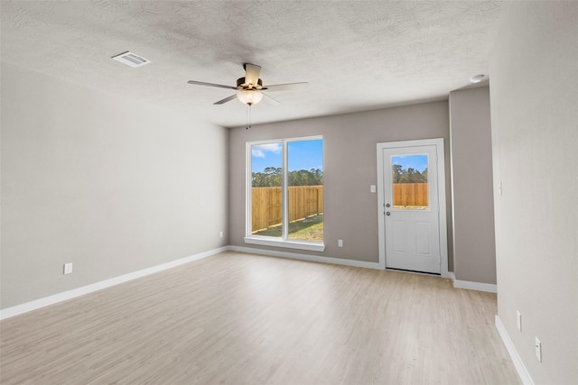 empty room featuring light wood-style floors, baseboards, visible vents, a ceiling fan, and a textured ceiling