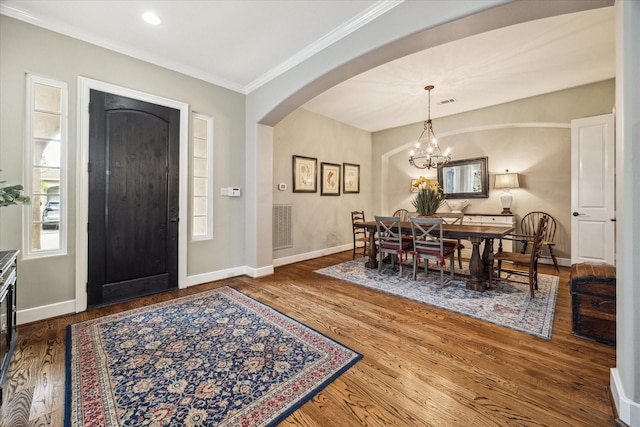 foyer featuring crown molding, arched walkways, baseboards, and wood finished floors
