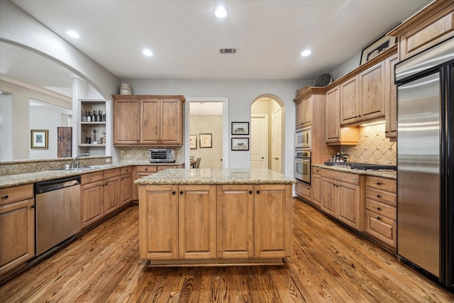kitchen featuring a sink, built in appliances, a center island, visible vents, and dark wood-style floors