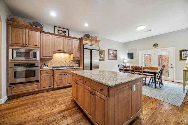 kitchen with built in appliances, a center island, light wood-type flooring, tasteful backsplash, and visible vents