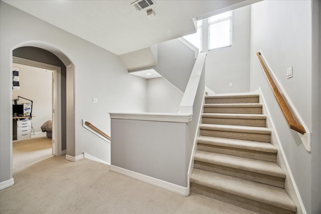 staircase featuring arched walkways, baseboards, visible vents, and carpet