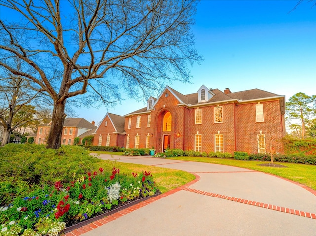 colonial-style house featuring a chimney and brick siding