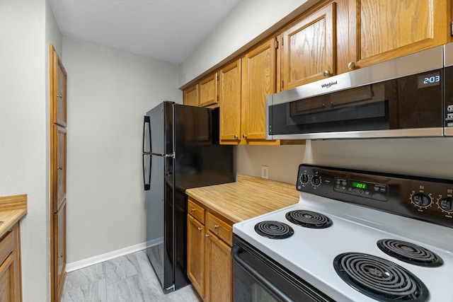 kitchen with freestanding refrigerator, stainless steel microwave, light countertops, marble finish floor, and electric range oven