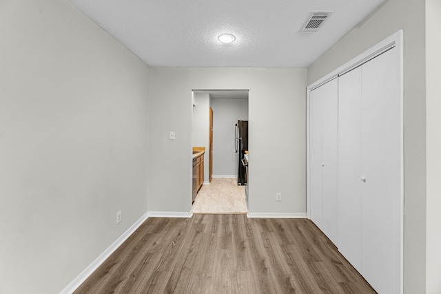 unfurnished bedroom featuring light wood-style floors, a closet, visible vents, a textured ceiling, and freestanding refrigerator